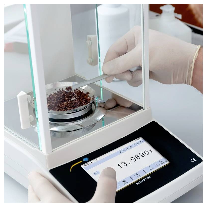 Rukavicemi opatřené ruce obsluhu digitální přesné váhy, která váží malý vzorek v laboratorním přístroji.