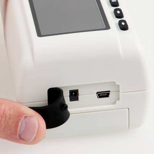 Prst zvedá gumový kryt USB portu bílého elektronického zařízení, aby odhalil samotný USB port.