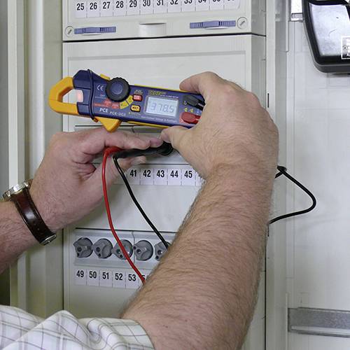 Osoba používá multimetr k provedení elektrického měření na rozvodné skříni.