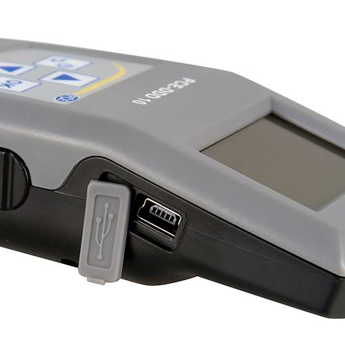 Detailní záběr elektronického zařízení s USB portem na boku. Zařízení má tlačítka a displej na horní straně.