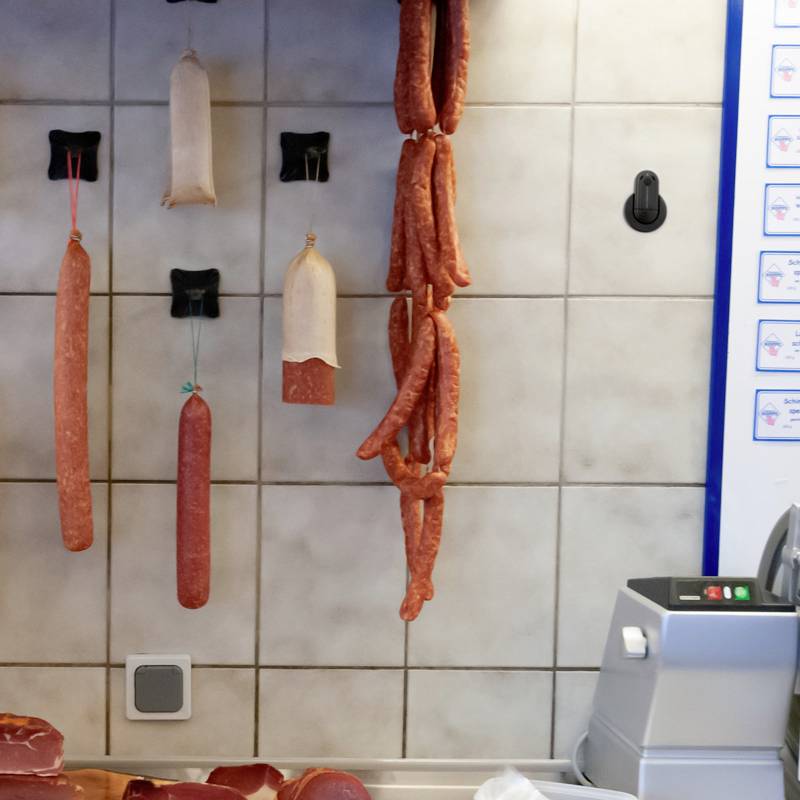 Různé druhy uzenin visí na háčcích na obložené stěně v řeznictví.