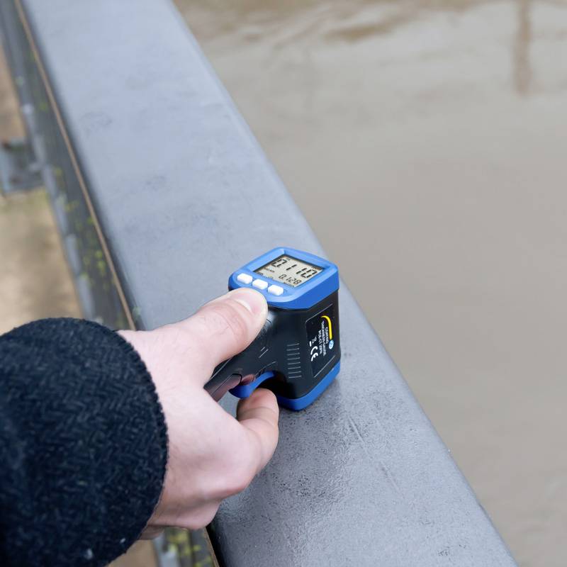 Jedna osoba drží laserový dálkoměr, který spočívá na zábradlí, a měří vzdálenost 27,10 metrů.