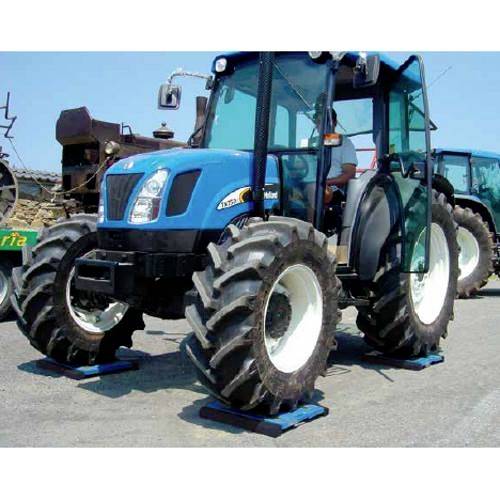 Modrý traktor s velkými koly stojí na asfaltové ploše. Podobné vozidlo je patrné v pozadí.
