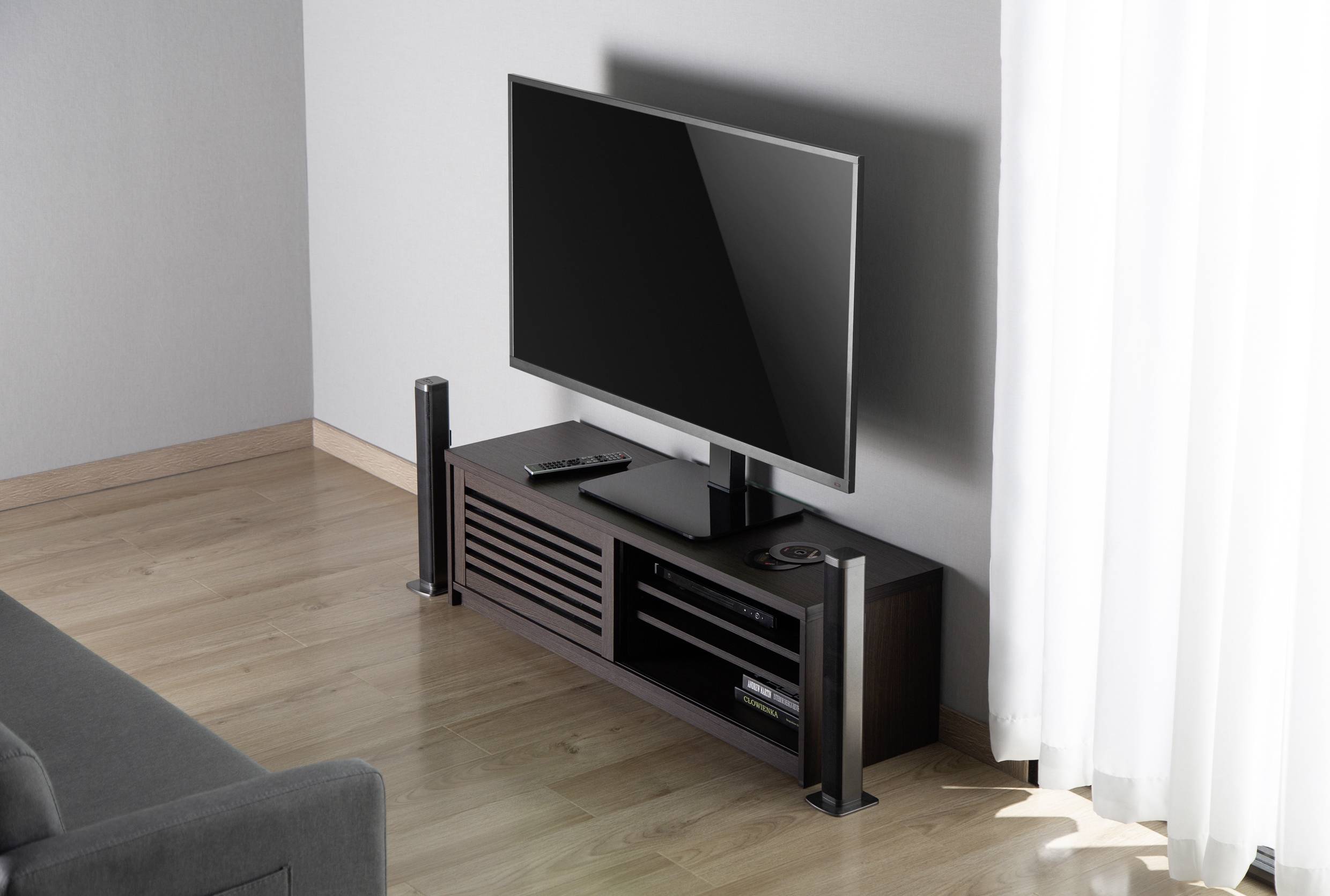 Plochý televizor na tmavém, moderním TV stolku s reproduktory a dálkovým ovladačem v světlém, minimalistickém obývacím pokoji.