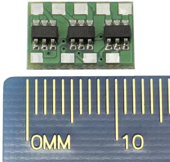 'Malá zelená součástka elektronického obvodu s šesti černými čipy, umístěná před pravítkem, které ukazuje délku 10 mm.'