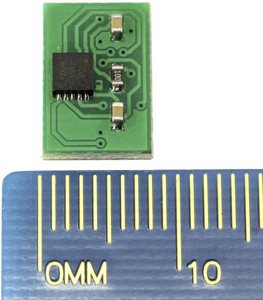 Zelený mikročipový modul nahoře, vedle modrého pravítka s milimetrovým měřítkem. Modul je přibližně 12 mm dlouhý.