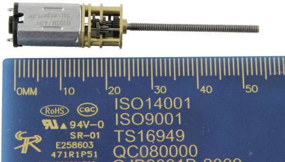 Malý elektromotor se závitovou tyčí, vedle něj modrá měřicí stupnice s certifikacemi jako ISO 14001, ISO 9001 a TS 16949.