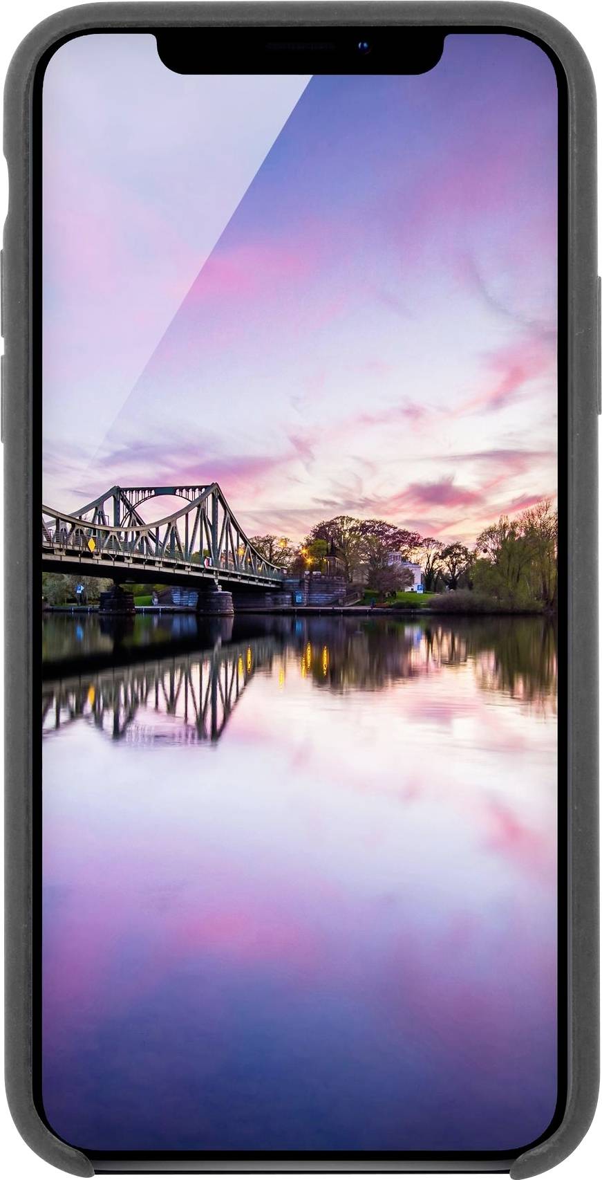 Mobilní telefon zobrazující pohled na řeku při západu slunce. Most se zrcadlí v klidné vodě a obloha je poseta růžovými mraky.
