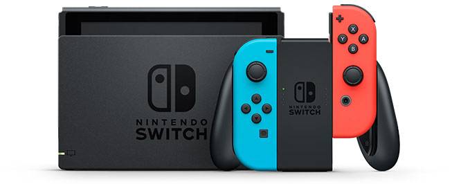 Nintendo Switch konzole s šedou dokovací stanicí a dvěma odnímacelnými ovladači Joy-Con v červené a modré barvě, na bílém pozadí.