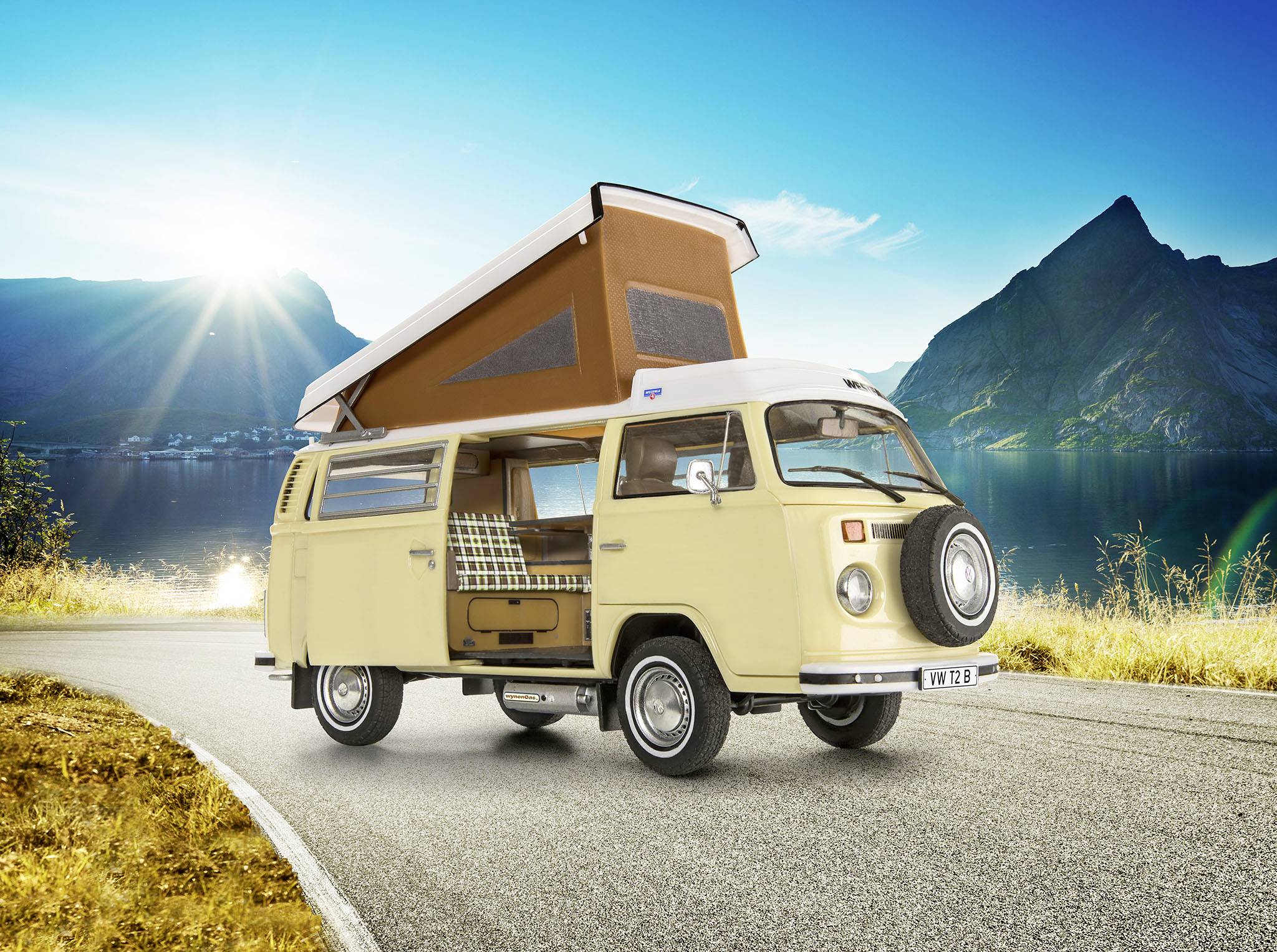 Béžový volkswagen bus se zvednutou střechou parkuje na venkovské silnici před horskou scenérií za slunečného dne.