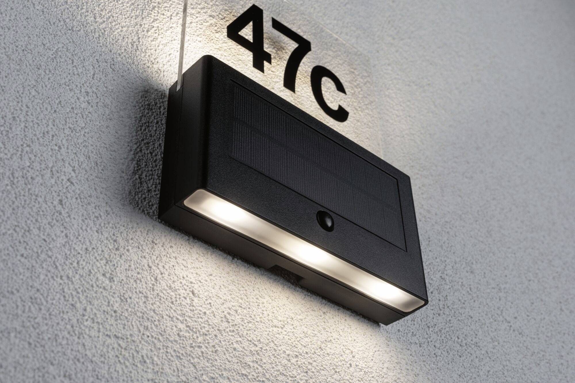Číslo domu 47C na zdi s venkovním osvětlením namontovaným pod ním.