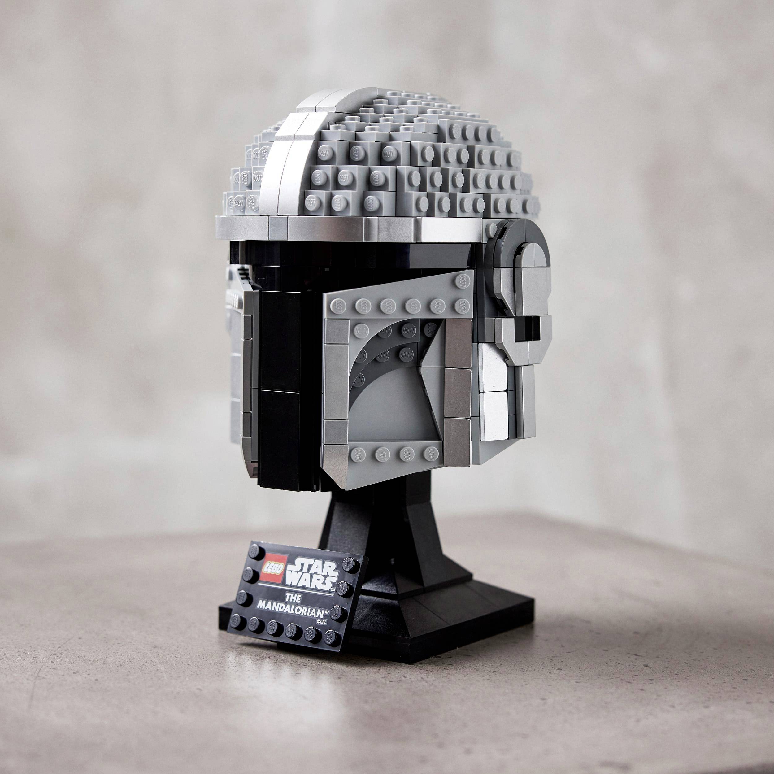 Sada LEGO modelu helmy Mandaloriana na stole. Helma je složená z šedých, černých a stříbrných dílků.