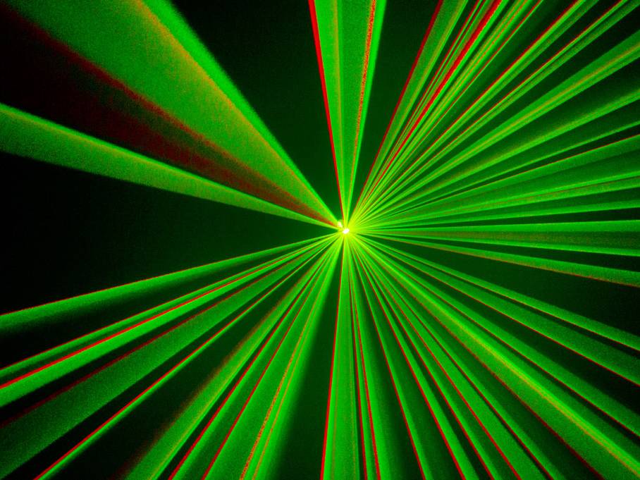 Zelené a červené laserové paprsky vytvářejí paprskovitý vzor na tmavém pozadí, který připomíná futuristický světelný design.