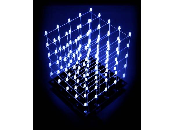 Modrý svítící 3D LED kostka stojící v temnotě na černé základně. Zobrazuje trojrozměrnou strukturu.