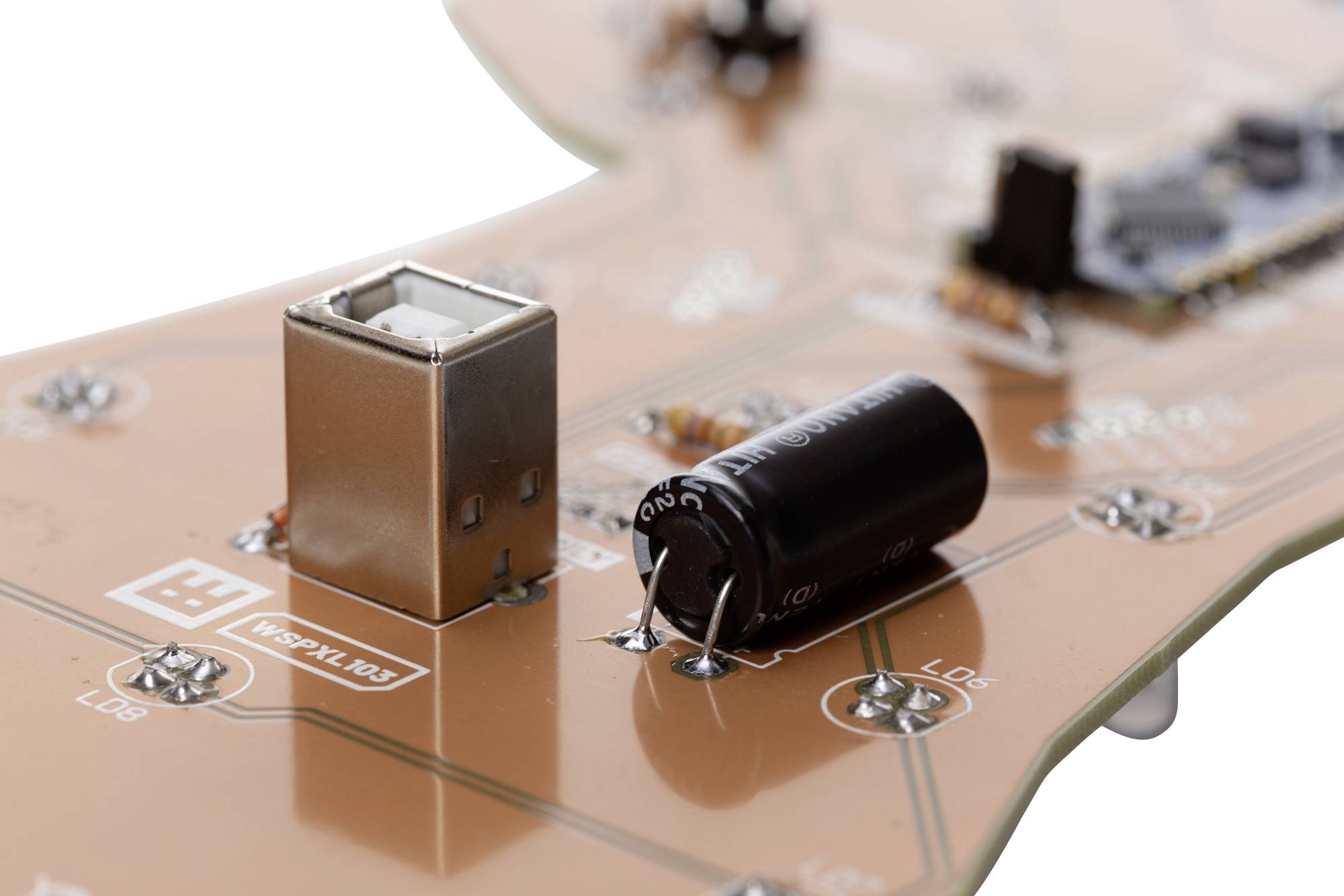 Detailní pohled na desku plošných spojů s elektronickými komponenty, včetně USB portu a kondenzátoru, na oranžové základní desce.
