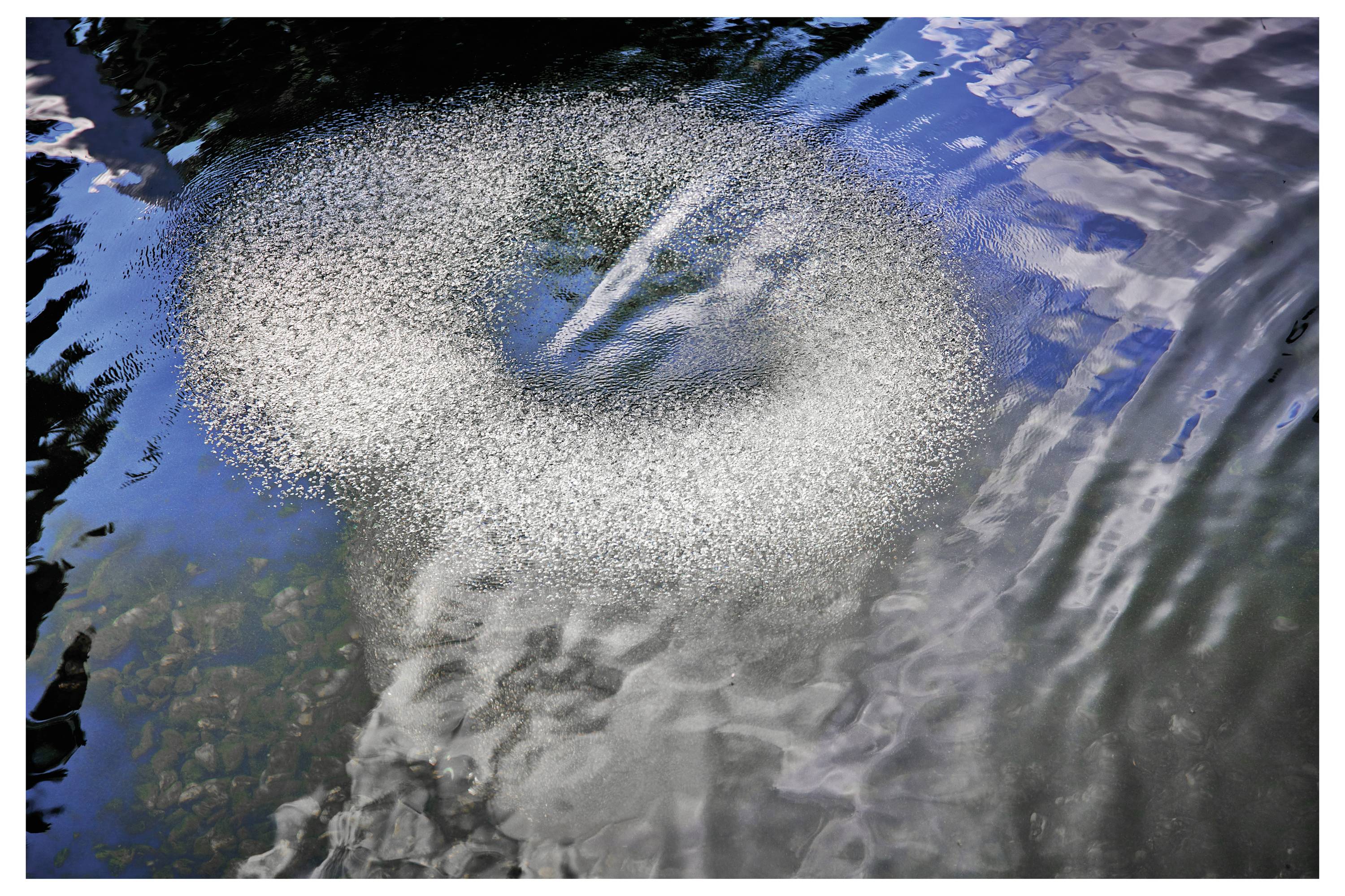 Kruhový vzor bublin ve vodě odrážející světlo a vytvářející spirálovitý efekt.