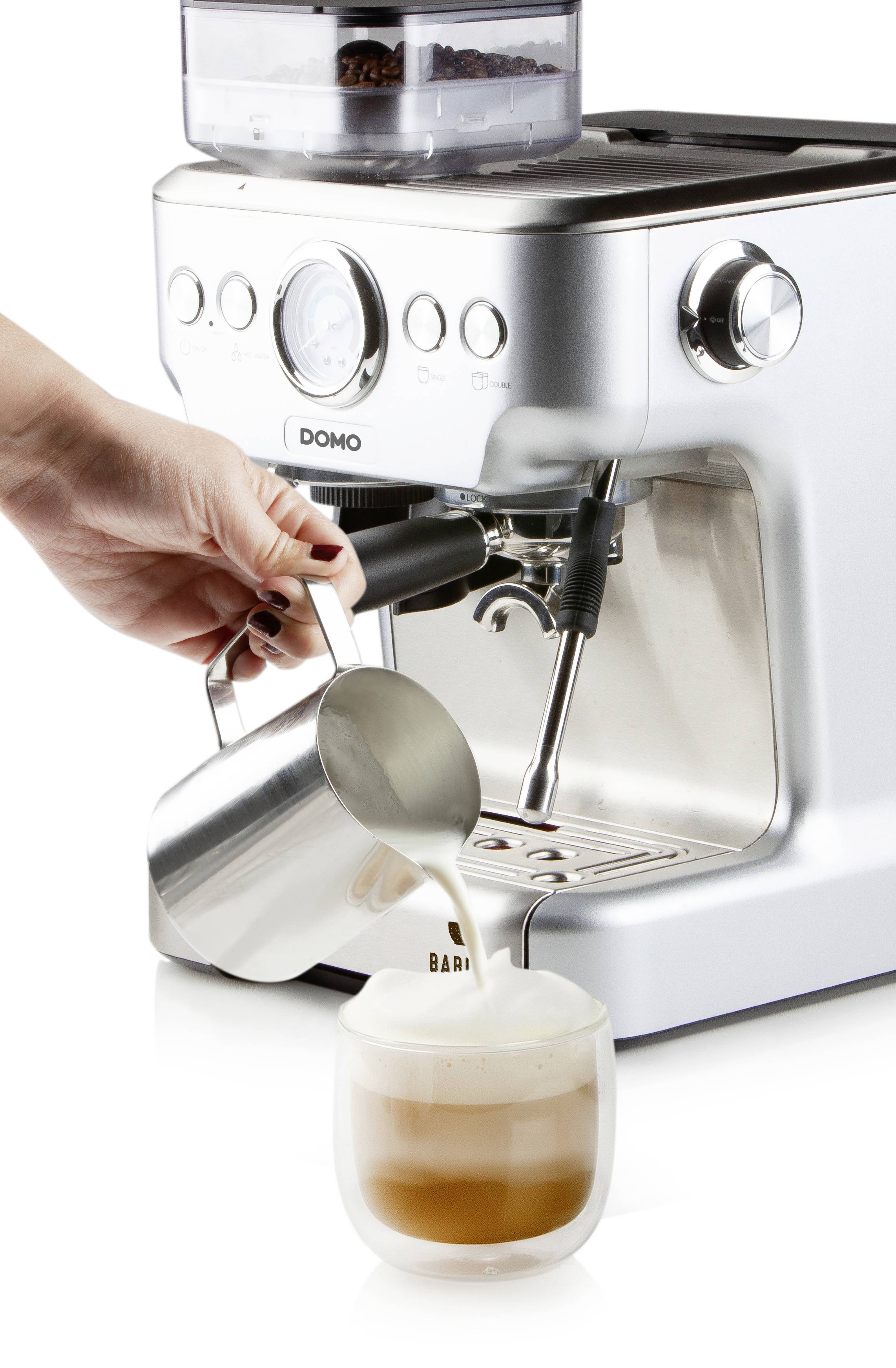 Osoba nalévá napěněné mléko do šálku s kávou vedle stříbrného espresso automatu.