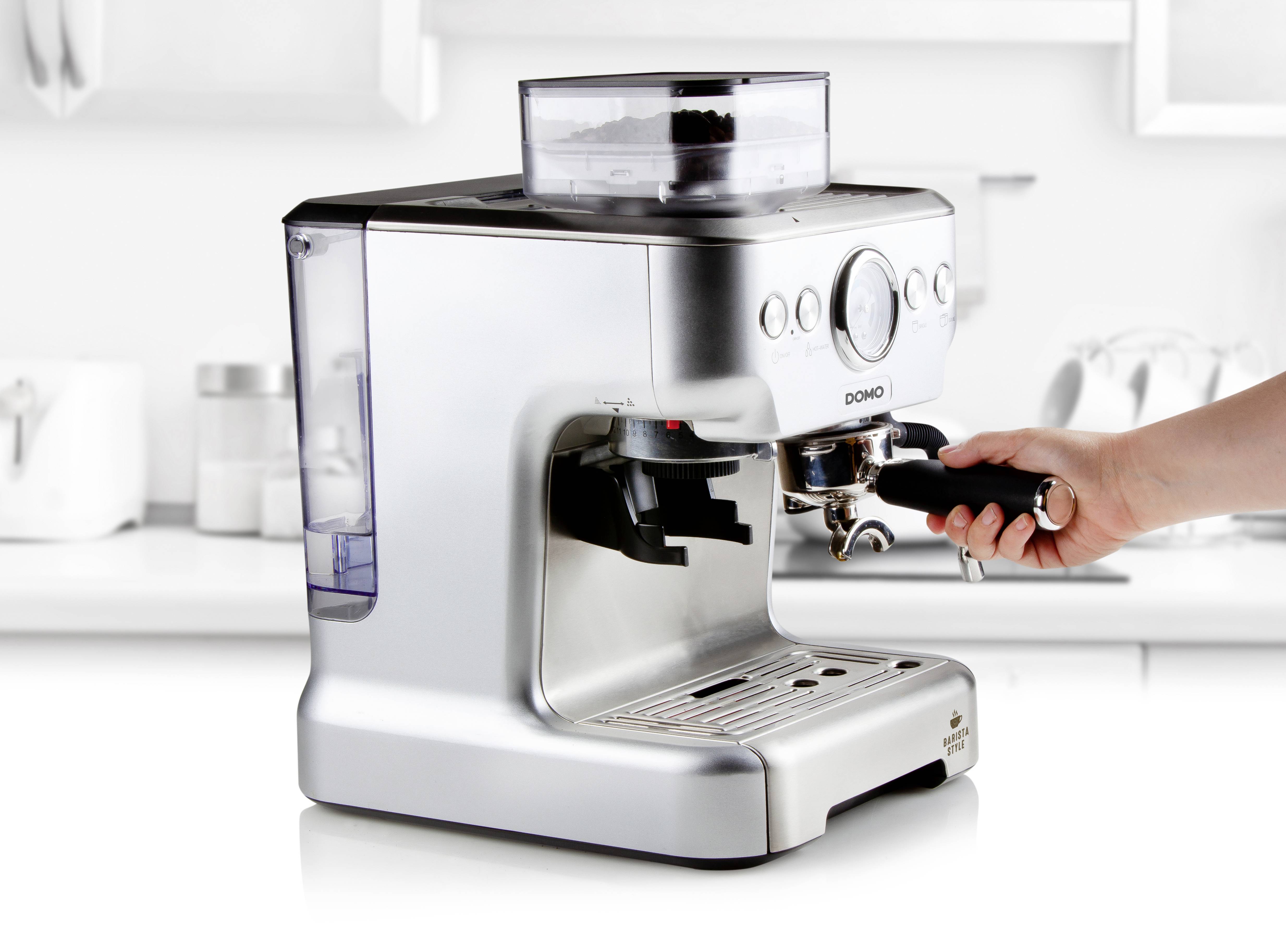 Stříbrný espresso kávovar v moderní kuchyni, ruka drží páku filtru.