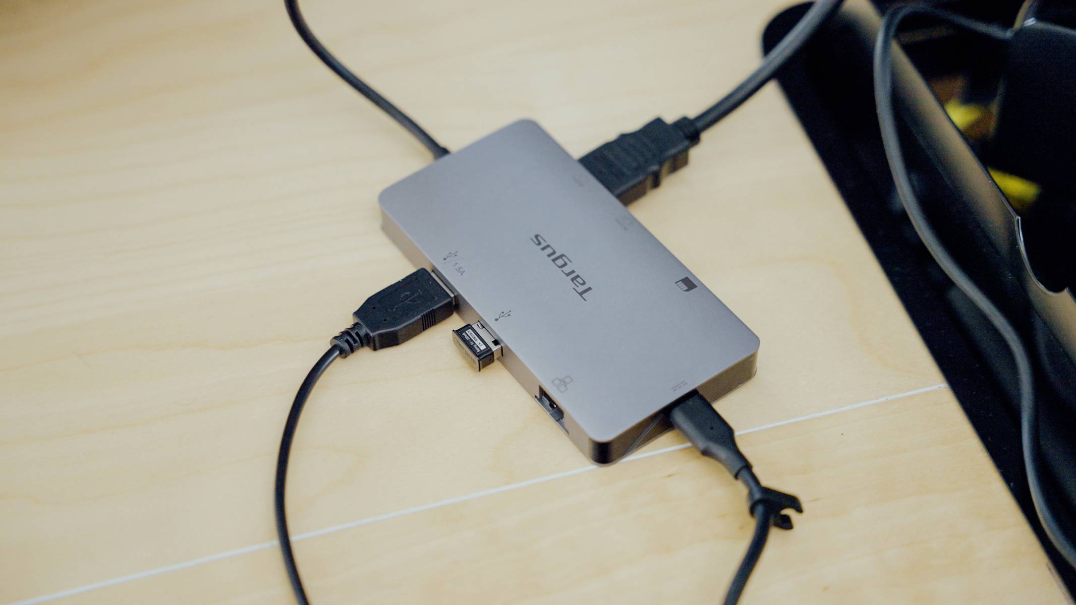 Kovový USB hub s několika připojenými kabely leží na dřevěném stole.