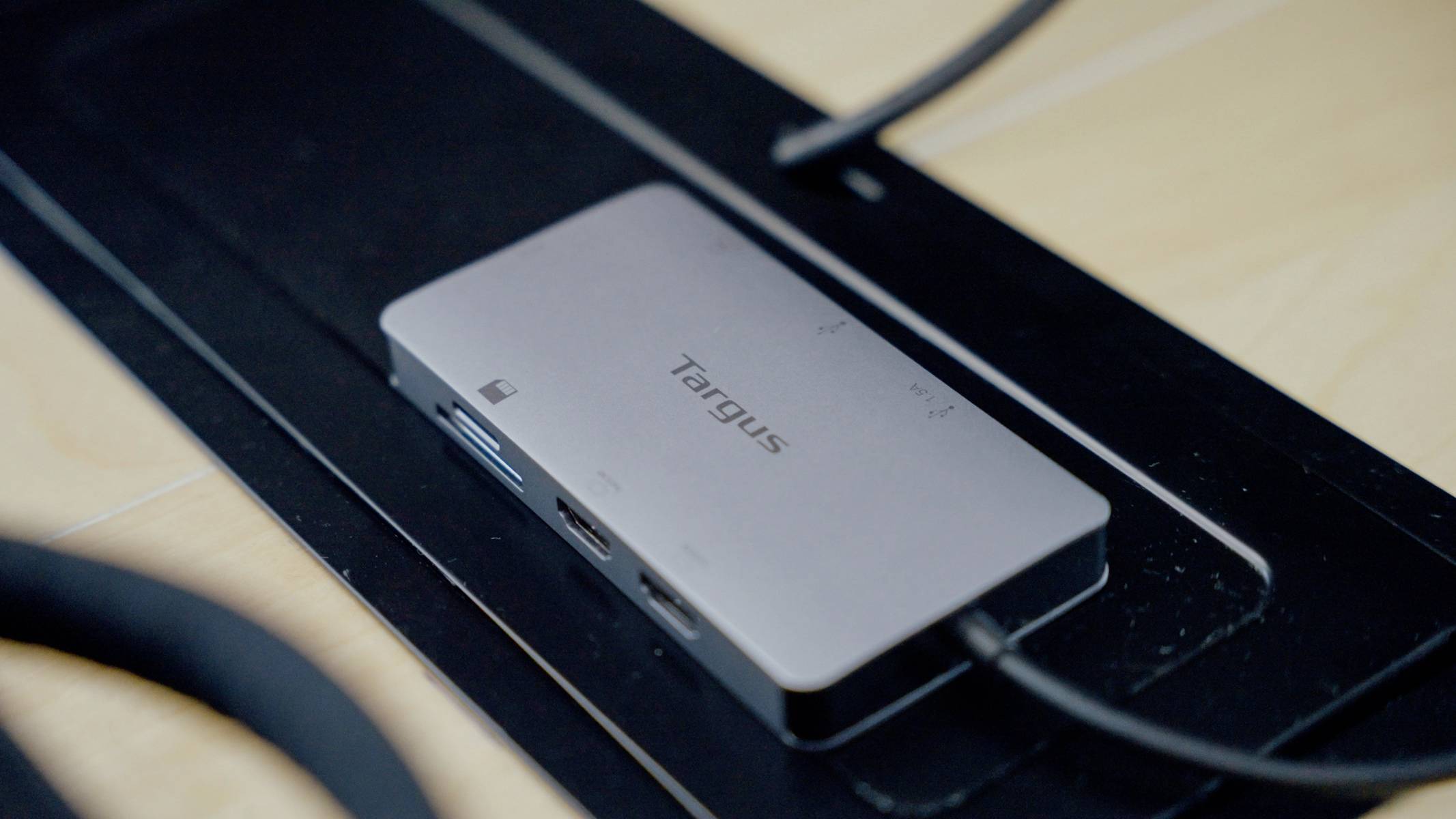 Na stole leží rozbočovač Targus USB, připojený k několika kabelům, který nabízí dodatečné USB porty pro elektronická zařízení.
