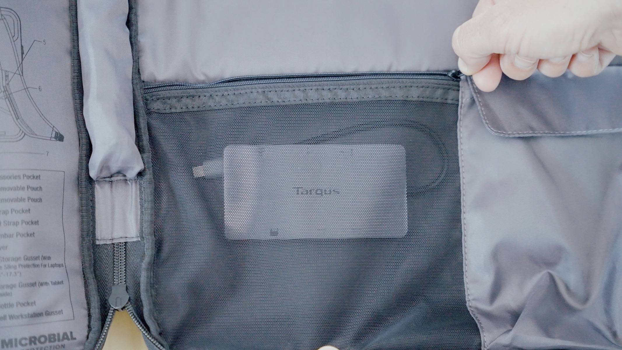 Otevřená taška s síťovým oddílem, ve kterém je uložen externí disk Targus. Jedna ruka drží zip otevřený.