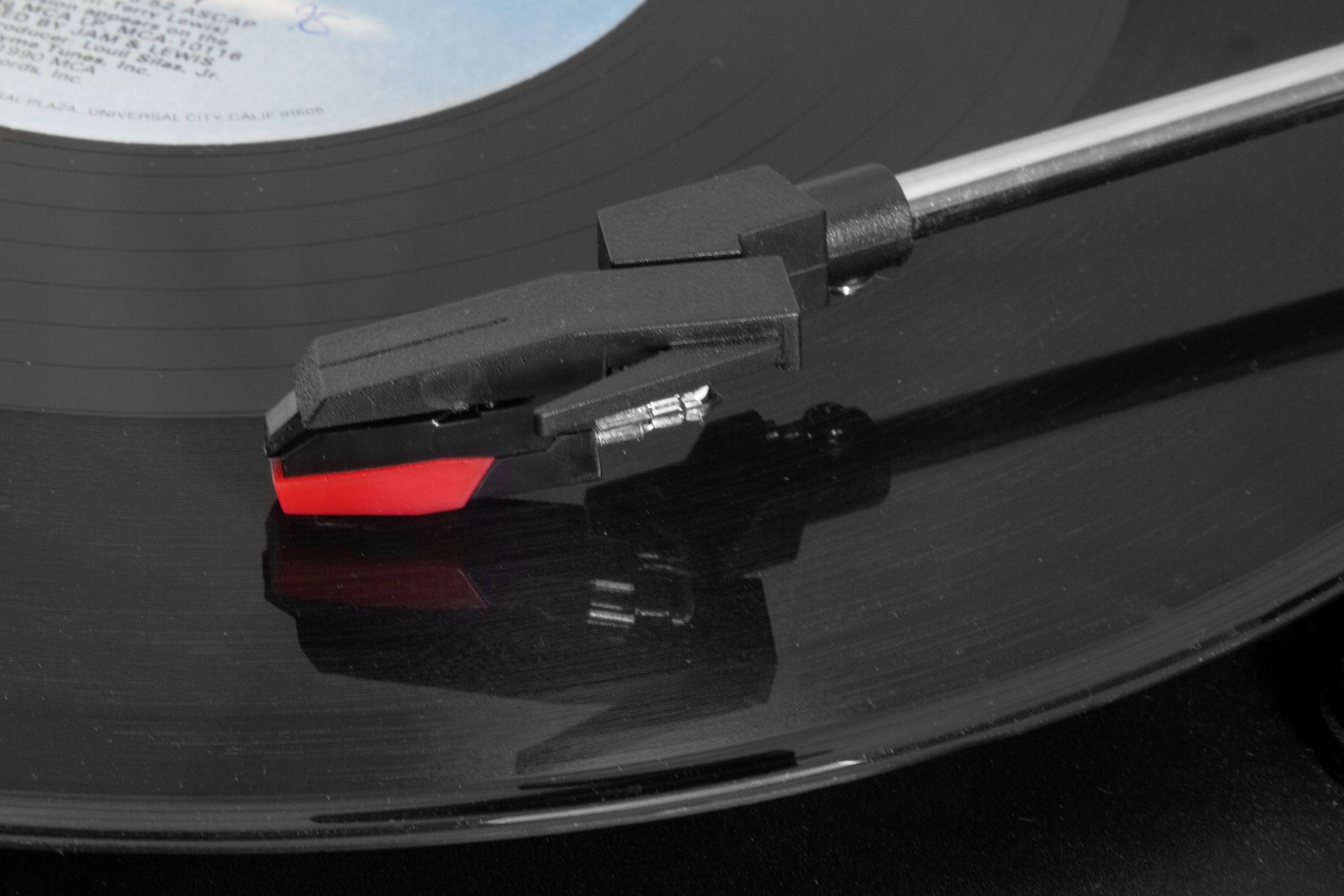 Jehla gramofonu se dotýká vinylové desky. Jehla je černá s červeným označením a zajišťuje zvukový výstup.