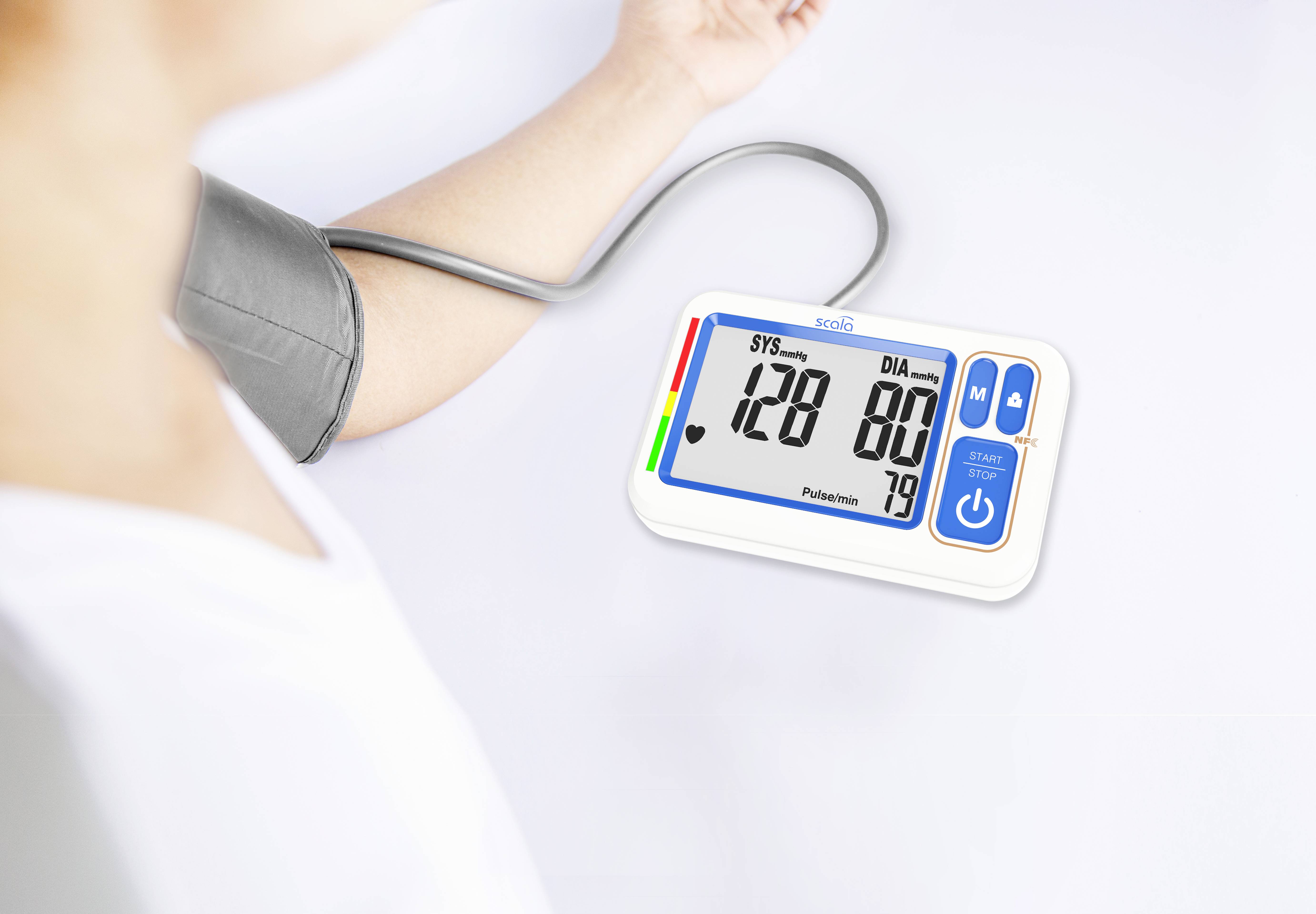 Osoba měří krevní tlak digitálním přístrojem. Display ukazuje 128 na 80 a puls 79.