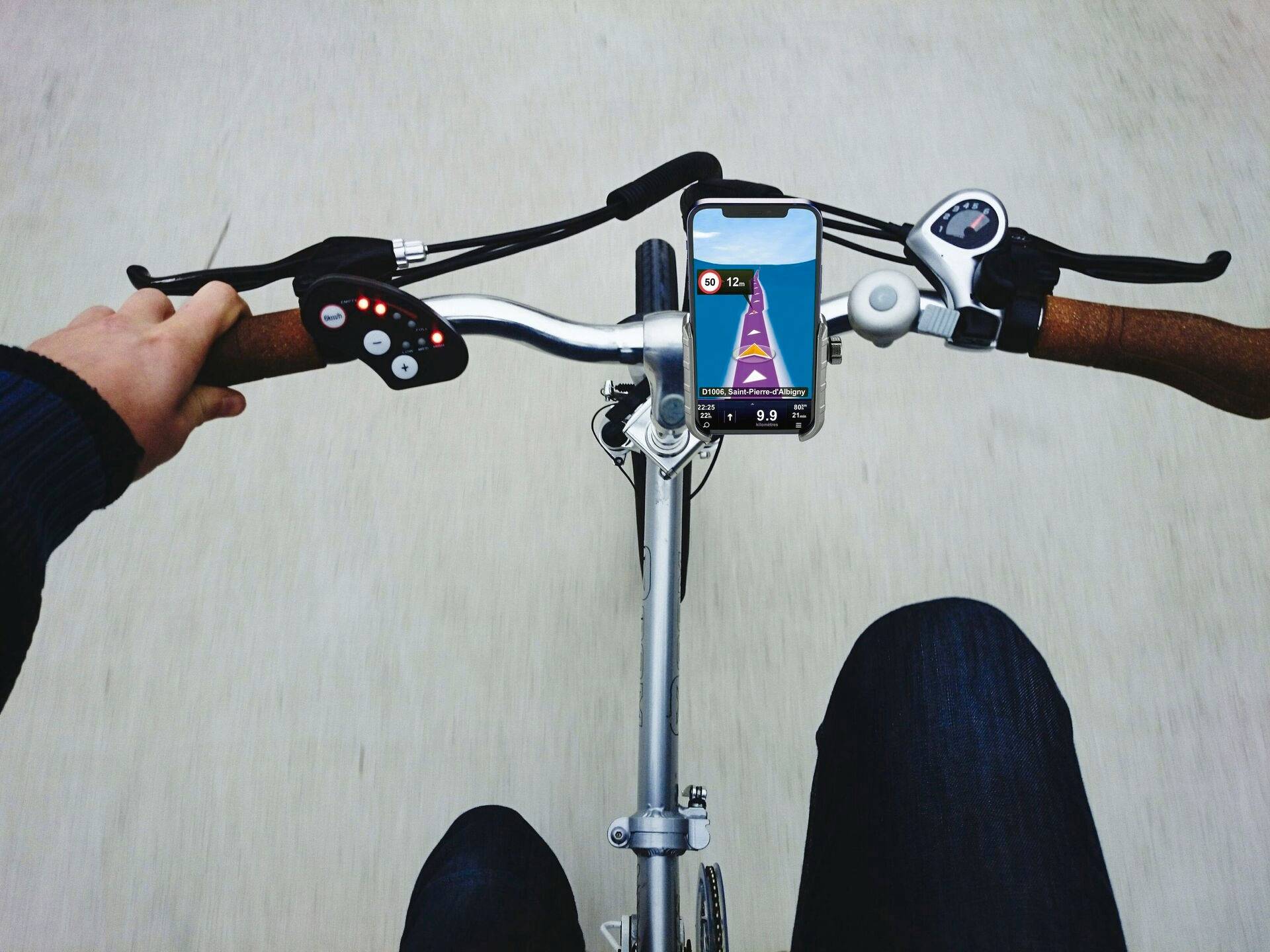 Pohled z pohledu první osoby cyklisty. Smartphone s navigační aplikací je upevněný na řídítkách.