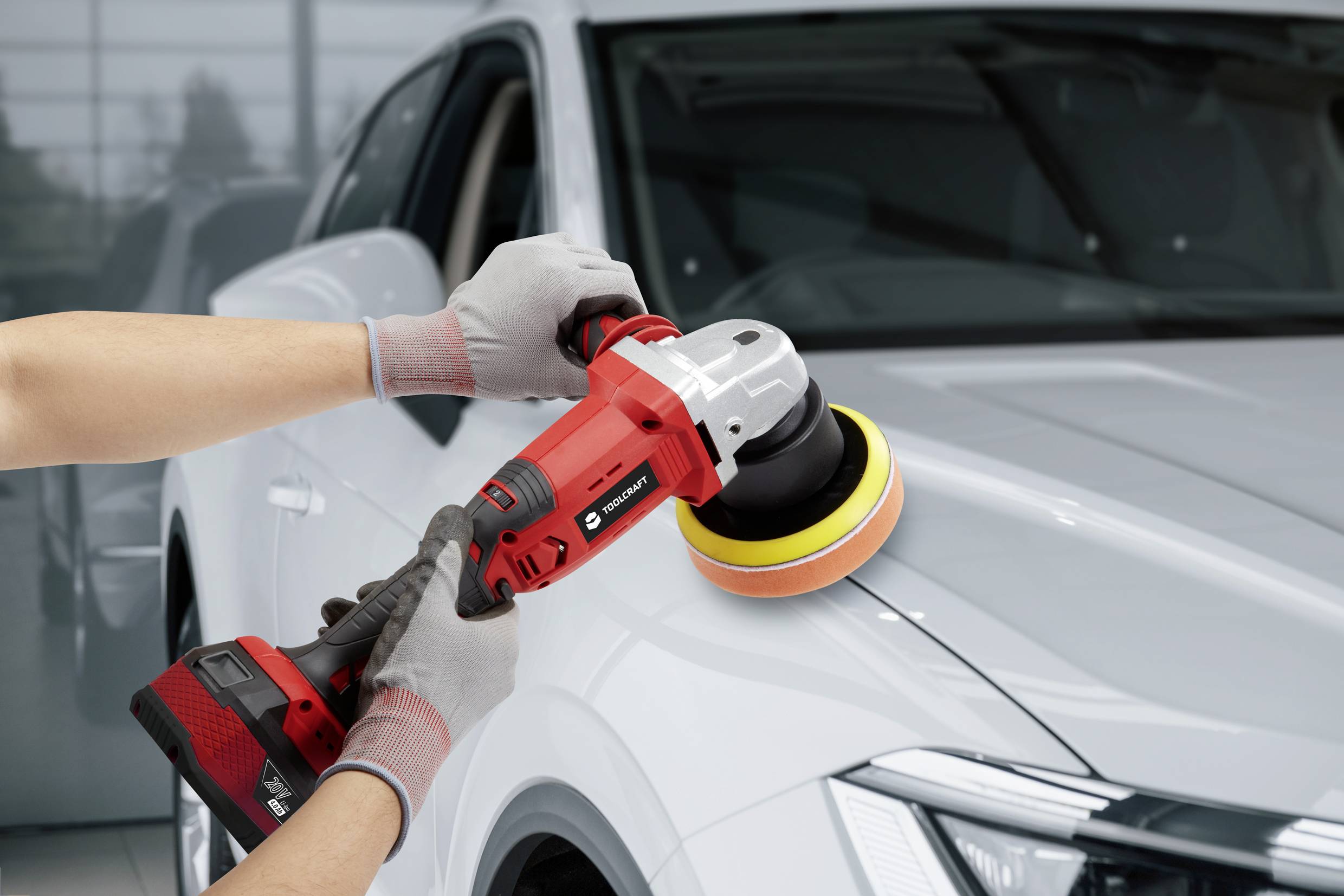 Člověk leští lak stříbrného automobilu červenou leštičkou v osvětlené garáži.