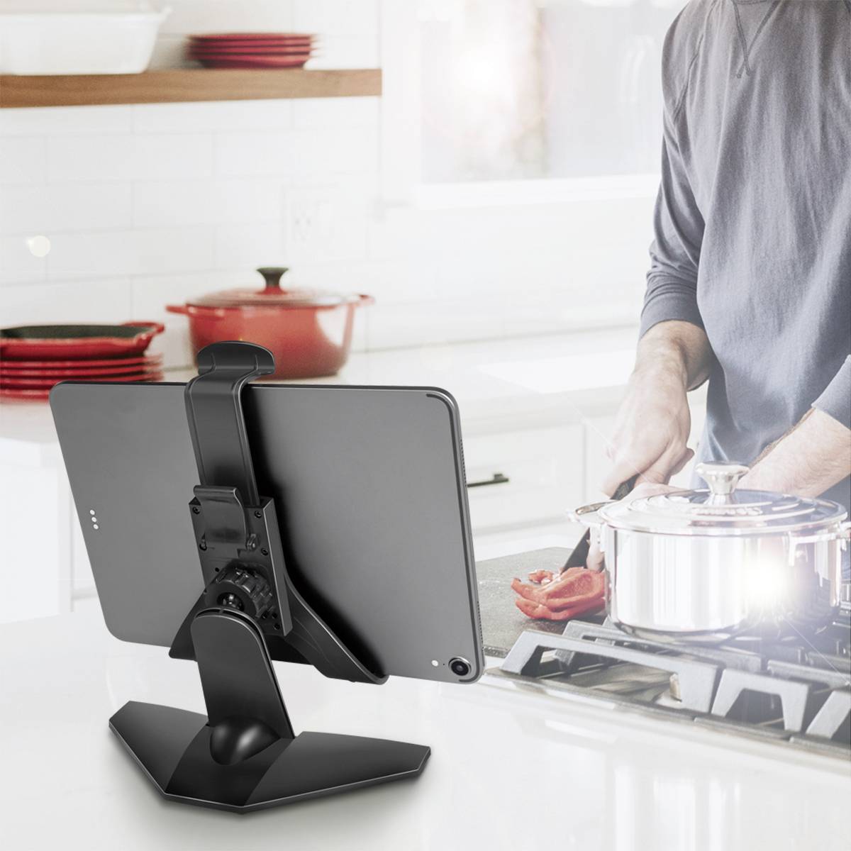 Osoba vaří v moderní kuchyni. Tablet je umístěn na stojánku a slouží jako průvodce receptem. V pozadí jsou kuchyňské pomůcky.