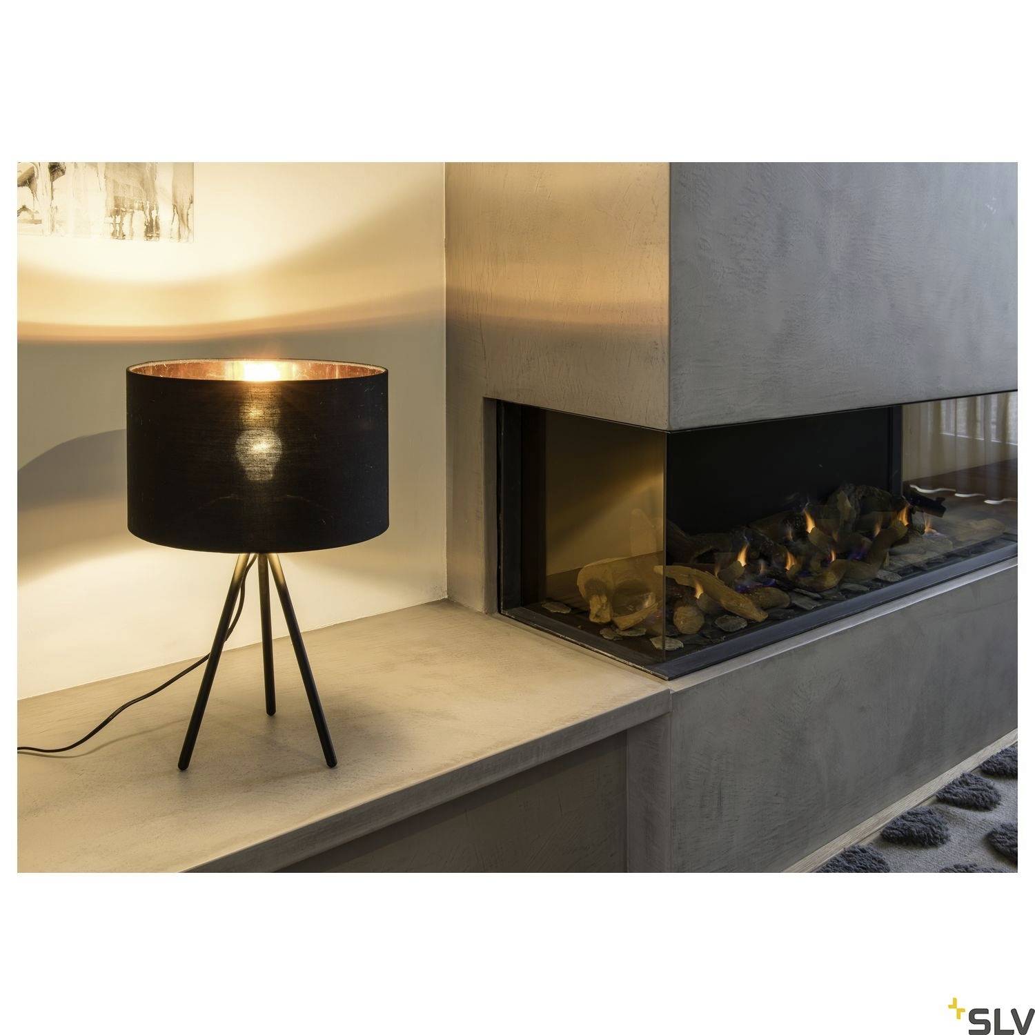 Stolní lampa s černým stínidlem na krbové římse vedle moderního zabudovaného krbu s hořícím ohněm.