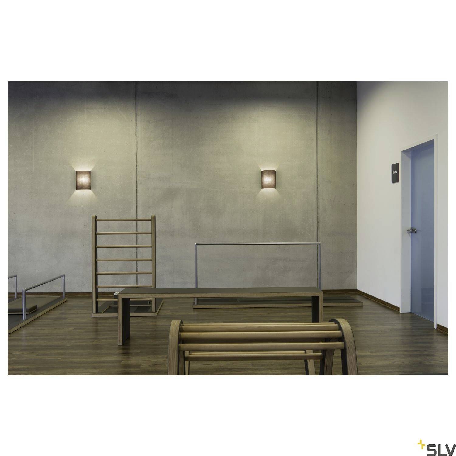 Minimalistický prostor s dřevěnou mříží na stěně a sedací lavicí, moderním osvětlením na šedých betonových stěnách, dřevěnou podlahou a dveřmi vpravo.