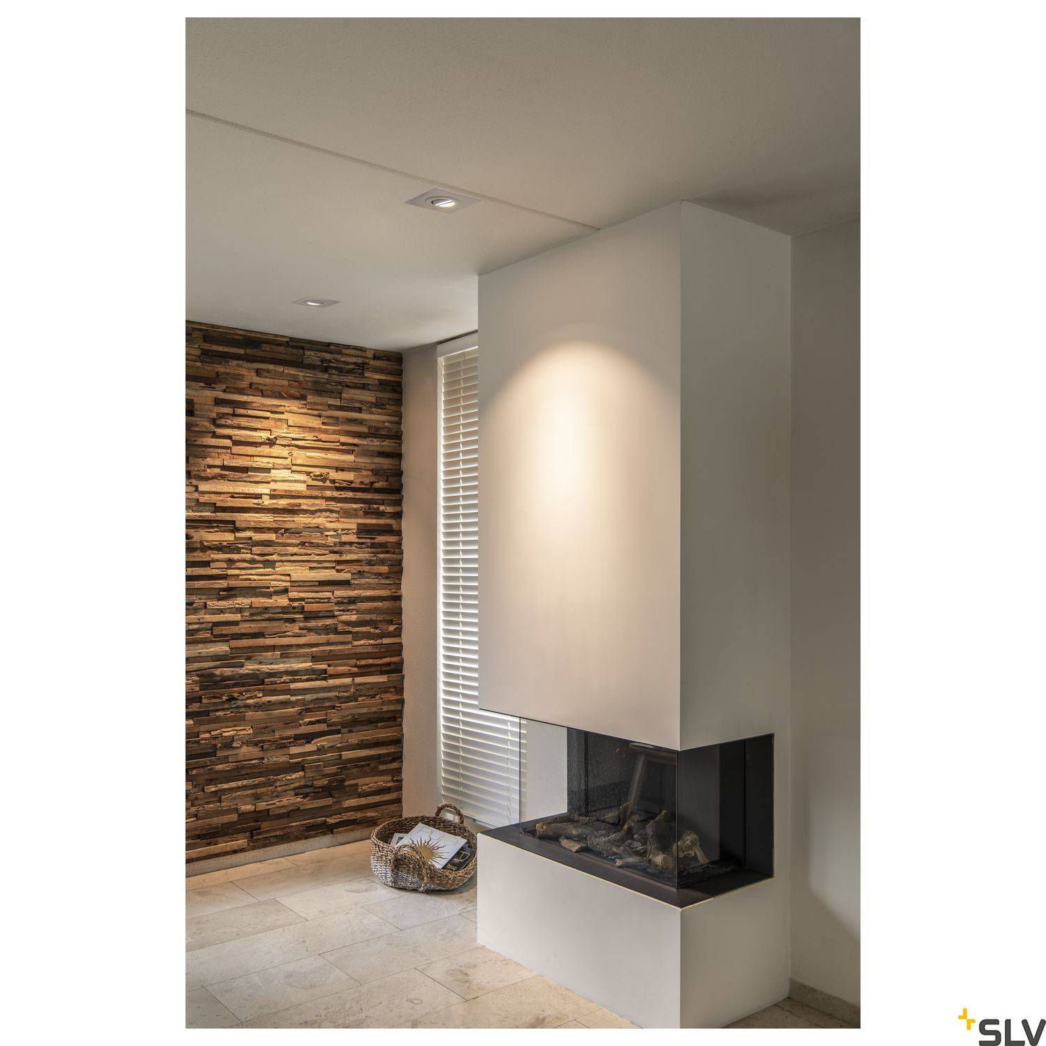 Moderní krb v obytném prostoru, obklopený kamennou stěnou a dekorací s košem. Měkké světlo osvětluje prostor.