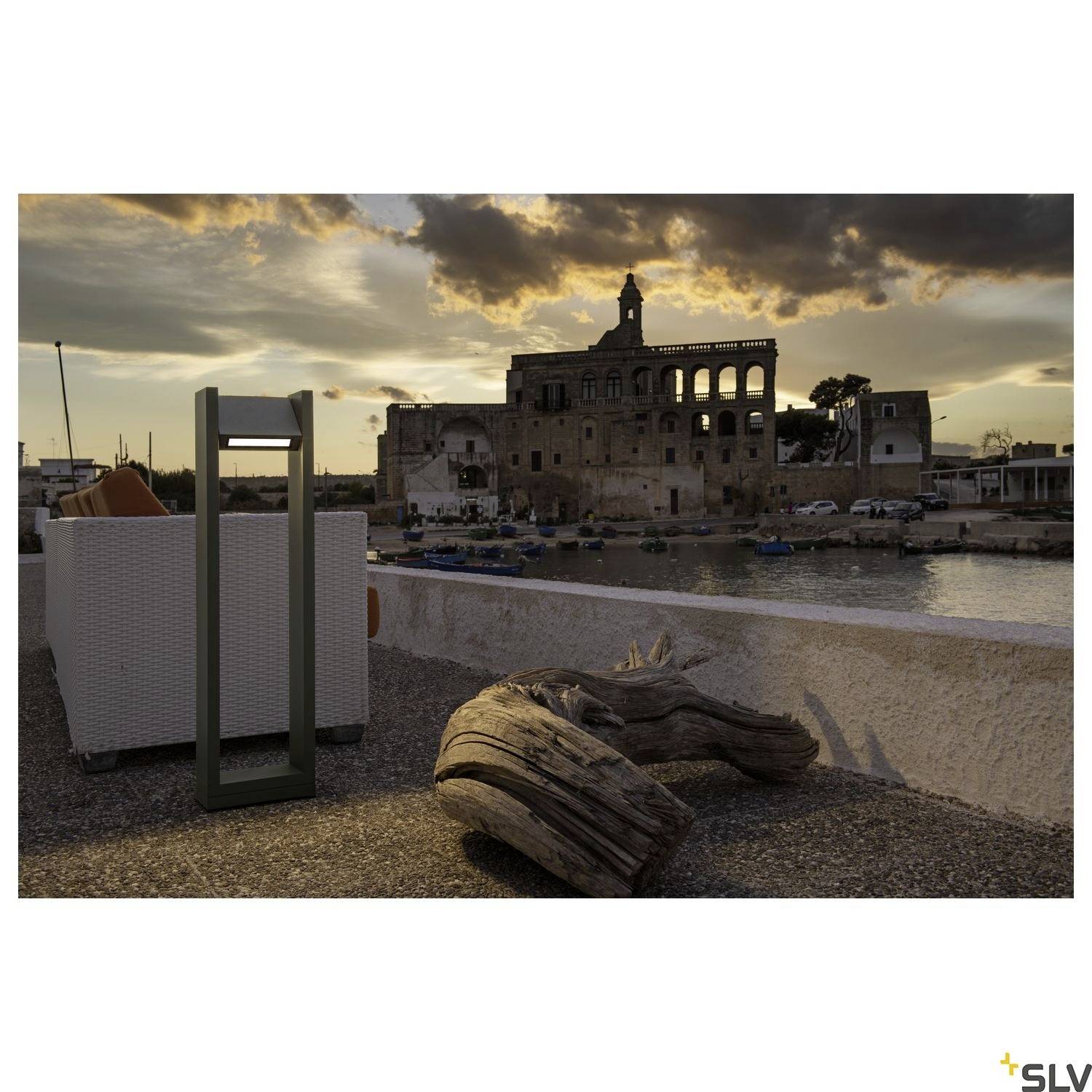 Večerní atmosféra v přístavu se starými kamennými budovami v pozadí. V popředí je vidět pouliční lampa a naplavené dřevo.