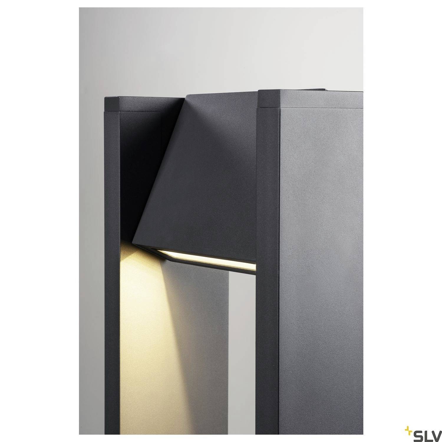 Moderní šedá venkovní lampa s geometrickým designem vyzařuje jemné světlo dolů a vytváří stínohru na stěně.