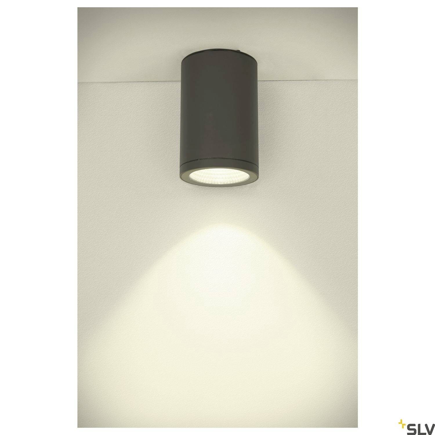 Válcové stropní svítidlo, které vysílá teplé bílé světlo na bílou stěnu. Energeticky úsporný design pro moderní interiéry.