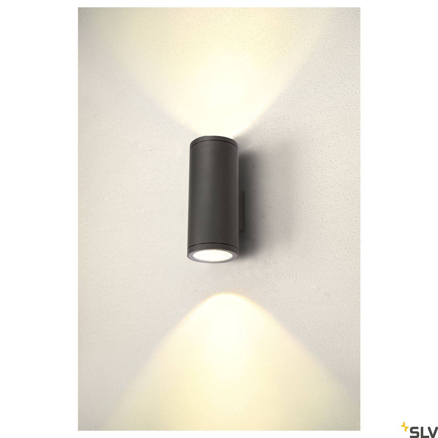 Nástěnná lampa válcovitého tvaru, upevněná na stěně. Světlo osvětluje prostor nahoru i dolů a vytváří elegantní atmosféru.