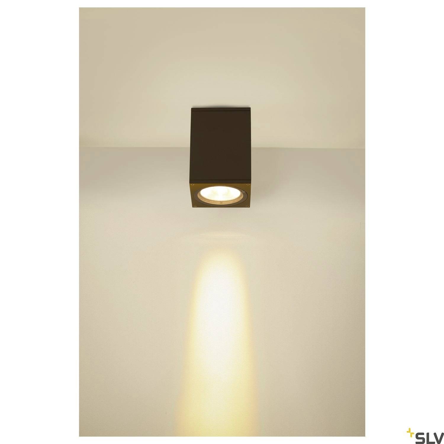Černé stropní svítidlo s teplým světelným paprskem směřujícím dolů v minimalisticky řešeném prostoru.