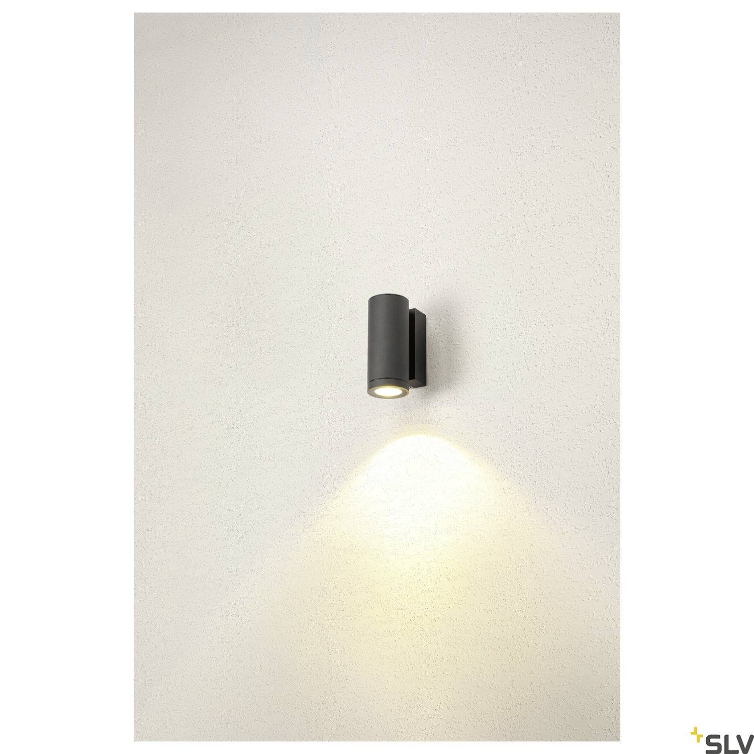 Černé nástěnné svítidlo promítá světlo dolů na krémovou stěnu, minimalistická moderní designová estetika.