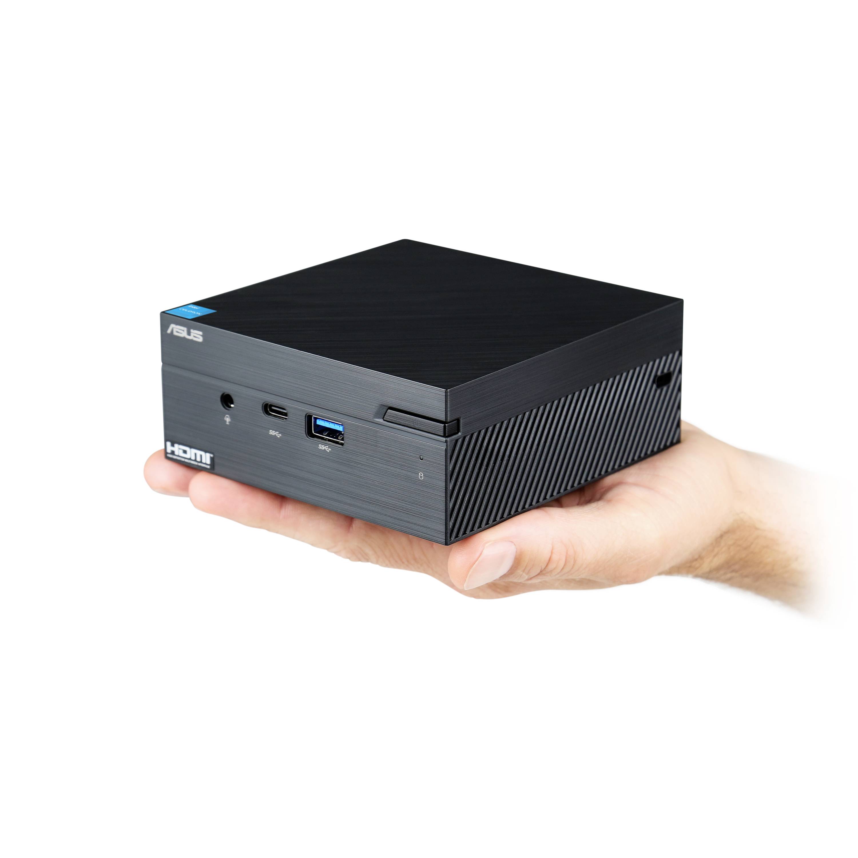 Jedna ruka drží kompaktní černý mini počítač od ASUSu s USB a HDMI porty na přední straně.