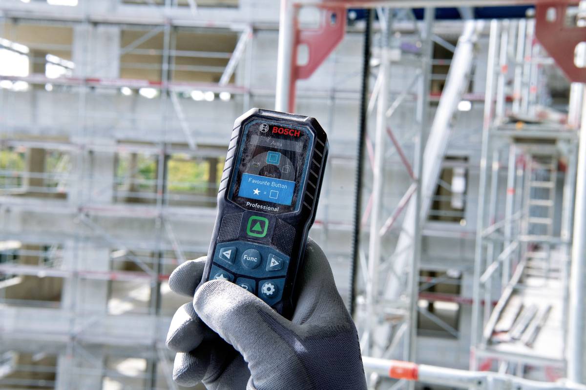 Osoba drží laserový dálkoměr Bosch při měření vzdálenosti v nedokončené ocelové konstrukční budově za účelem přesného určení vzdálenosti.