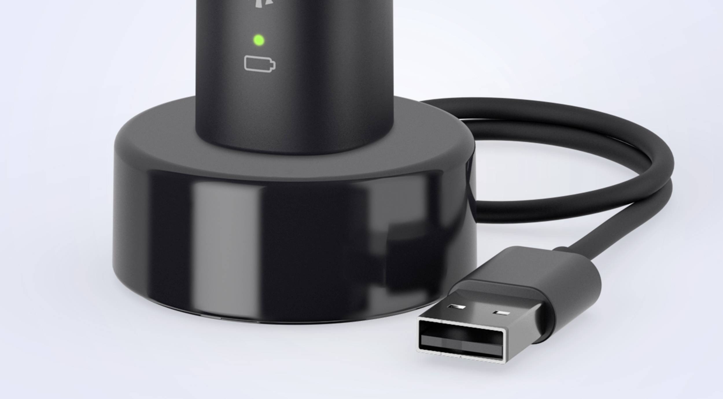 Černá nabíječka s podstavcem a USB kabelem. Zelené světlo signalizuje, že zařízení se nabíjí.