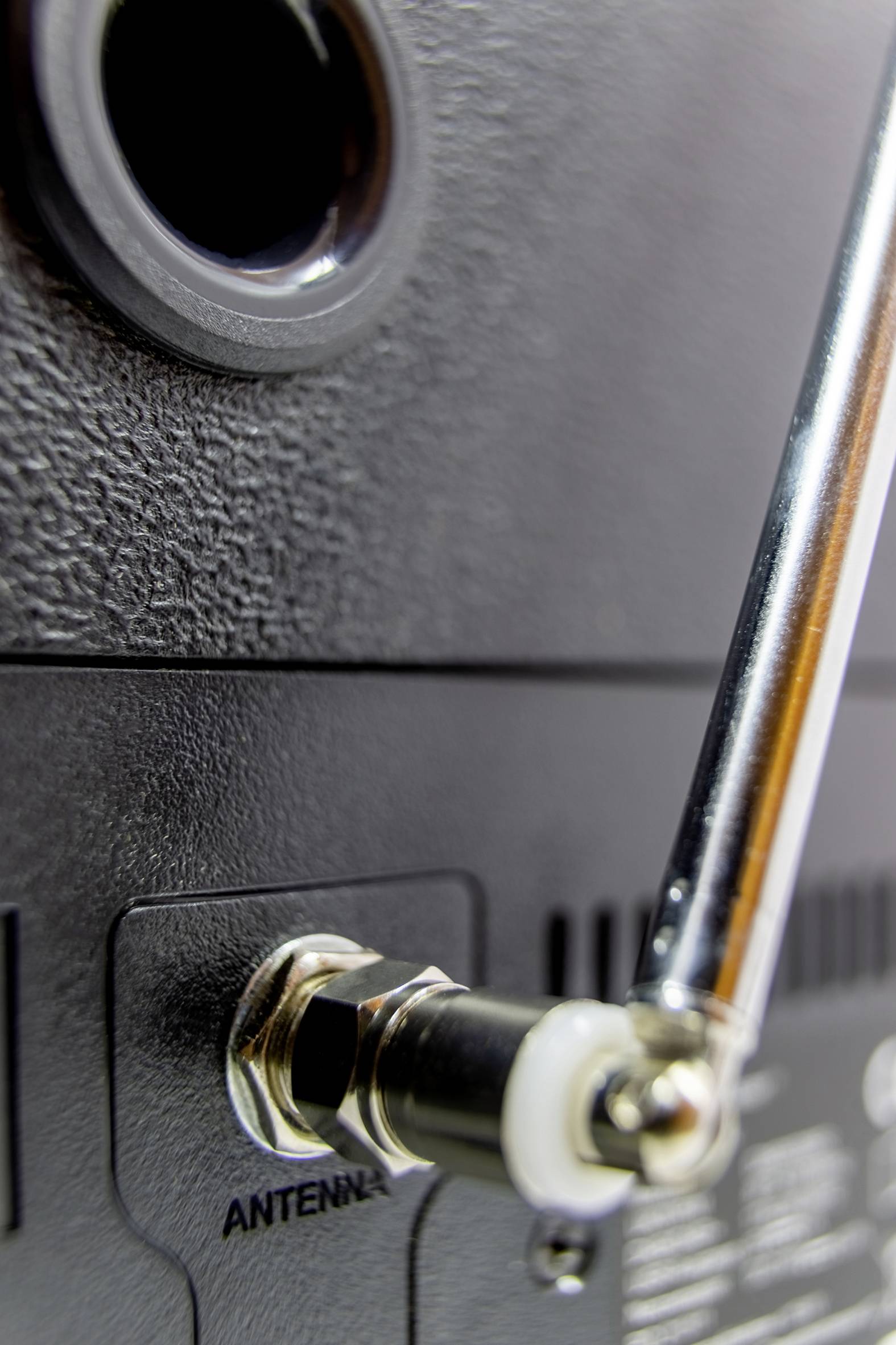 Detailní záběr radiostanice s připojenou anténou, zaměřený na anténní konektor a kovový spoj.