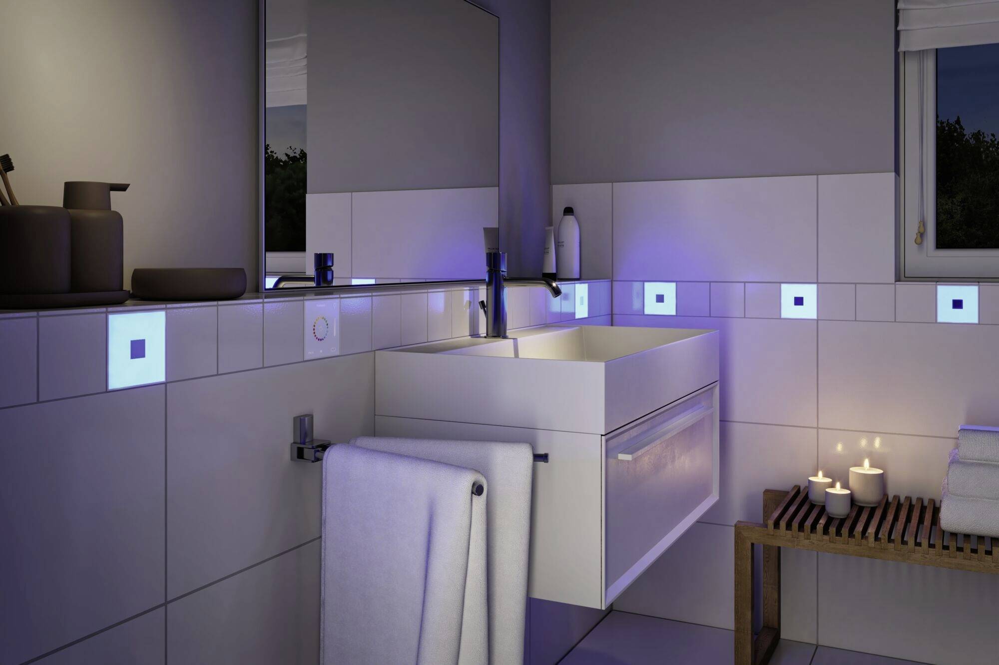 Moderní koupelna s bílým umyvadlem, obklopená osvětlenými modrými dlaždicemi. Ručníky visí na držáku na ručníky.