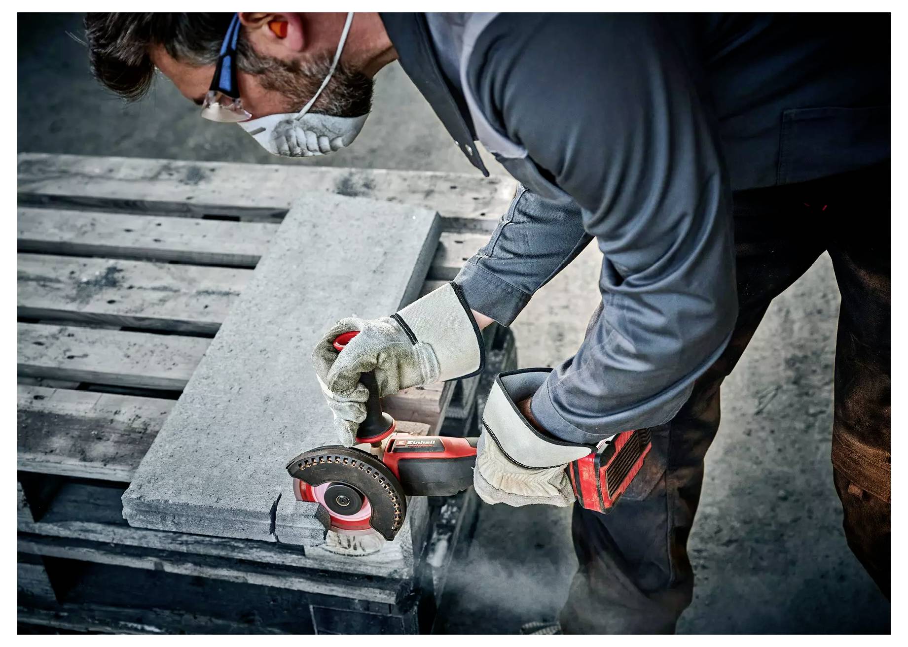 Osoba v bezpečnostní výstroji brousí betonový blok pomocí elektrického nářadí na dřevěné paletě, což ilustruje nástroje používané ve stavebnictví.