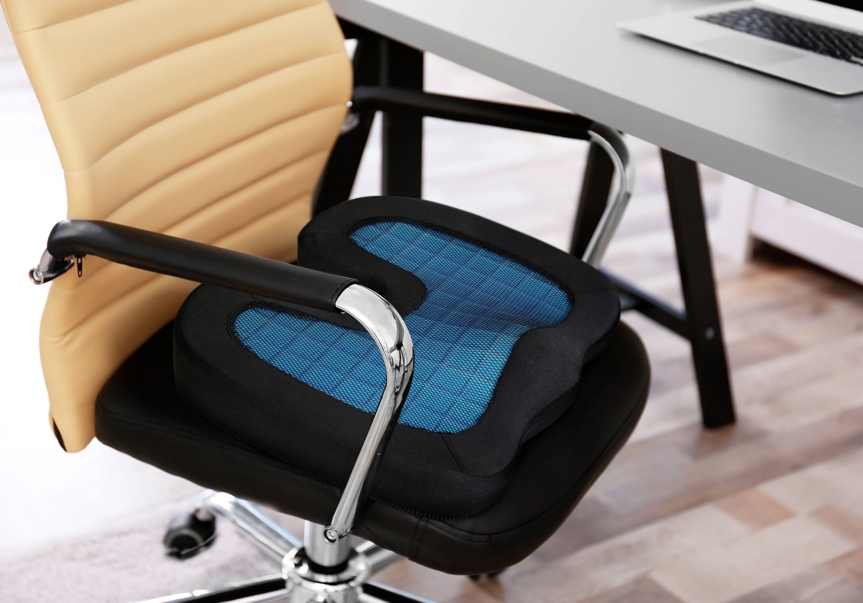 Ergonomický podsedák na kancelářské židli před stolem s laptopem, který zlepšuje pohodlí a postoj při sezení.