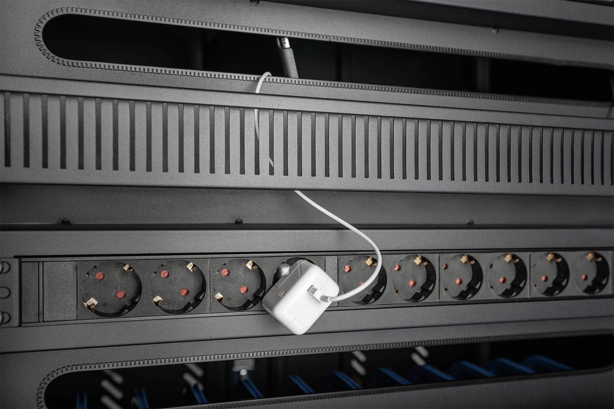 Síťový kabel je připojen k adaptéru, který je zapojen do řady černých zásuvek v serverovně.