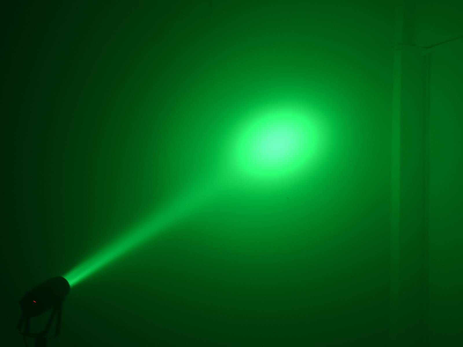 Zelený světelný kužel z reflektoru osvětluje stěnu v tmavém prostředí.