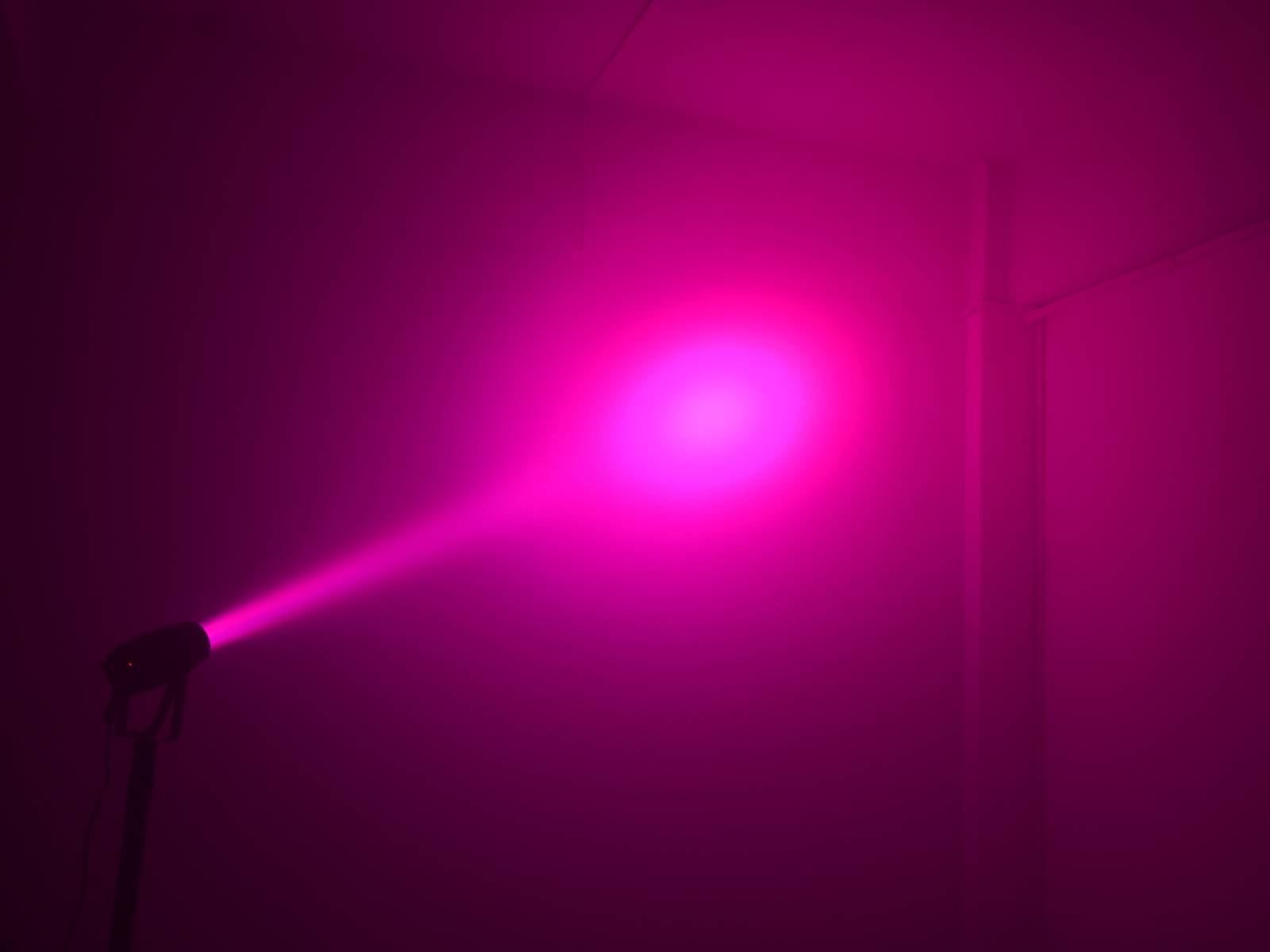 Silné červené světlo vyzařuje z projektoru v tmavém rohu, osvětluje stěnu a vytváří intenzivní, barevnou atmosféru.