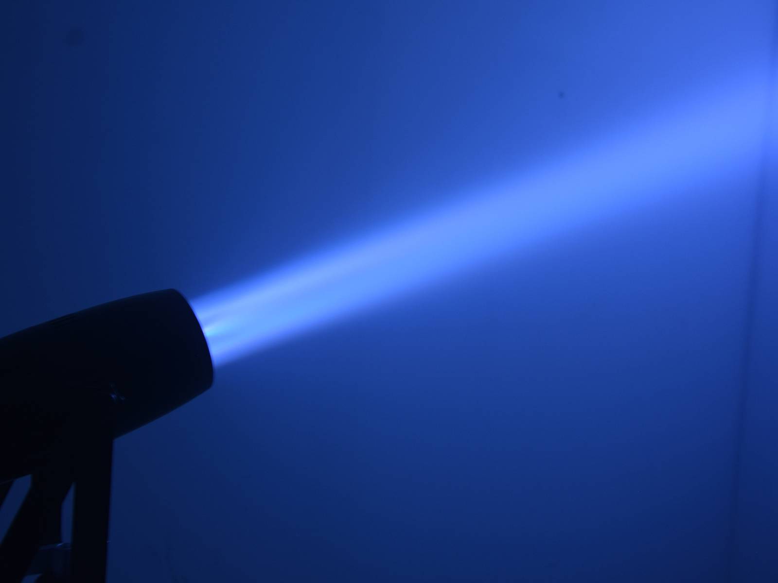 Lampa vyzařuje intenzivní modrý světelný paprsek v tmavé místnosti.